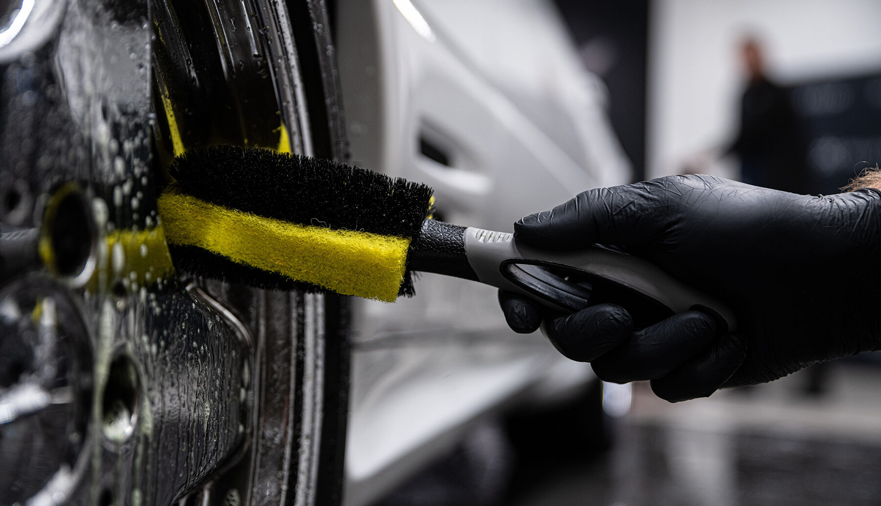 car wash or car detailing studio employee washes a shiny chrome rim