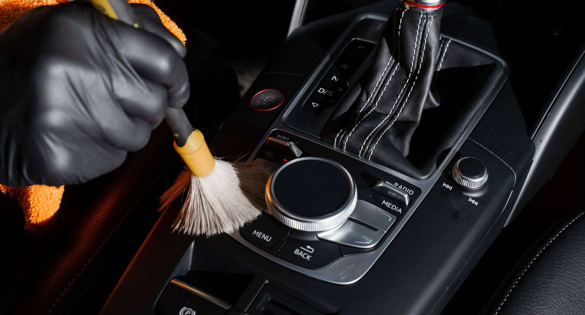 Dry cleaning with brush of gearbox and dashboard in car. Auto detailing service. Cleaning individual elements of black leather interior in auto.
